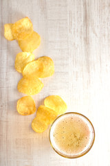 a glass of cold, light beer with chips scattered on the table. copy space. top view on light wooden background.