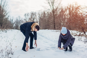 Fototapeta na wymiar Beautiful loving couple picking some snow to play snowballs in winter forest together. People having fun outdoors
