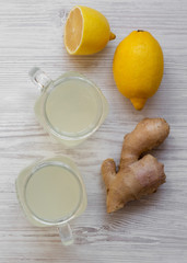 Glass jars of homemade ginger tea with lemon over white wooden surface, top view. Flat lay, from above, overhead. Closeup.