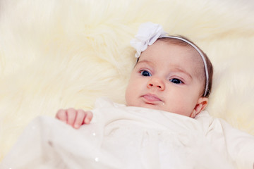 little baby on a light fur in white dress with a bow in the hair