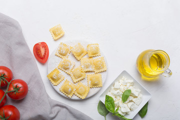 Raw ravioli with basil, cheese and tomatoes on white background, top view