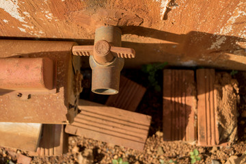 Rusty Water Turbine Generator and Vintage Old PVC Valve with Plastic Pipeline - Moldy Concrete Wall Texture - Dirty Bricks on Sandy Ground