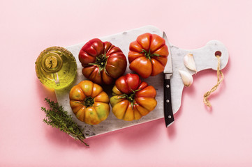 brandywine tomato on a cutting board. cooking summer salad with fresh olive oil, thyme. on a rose background