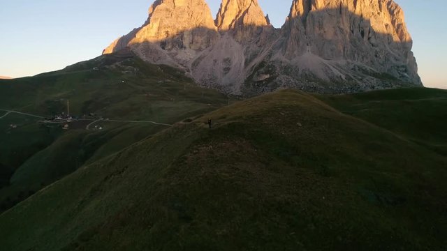 Woman standing on a hill, C4k aerial, drone shot, around a girl hiking on a hill, in front of Dolomiti mountains, at Sella pass, on a sunny, summer morning, in Dolomites, Tyrol, Italy