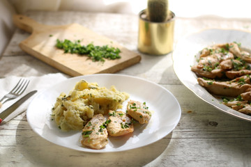 Grilled chicken with fresh parsley and mashed potatoes on a rustic white table. Selective focus.