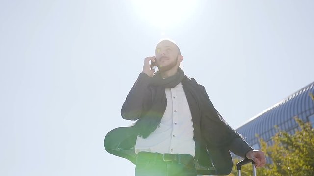 Caucasian businessman uses and talking on phone while he standing near the modern office building. Outdoors . Concept: office worker, business, business trip, advertising