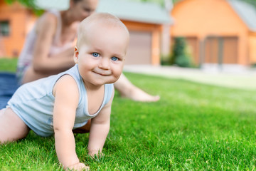 Portrait of cute little caucasian boy having fun in garden with mother. Child crawling on green grass lawn during walk with mom in yard. Happy childhood and baby healthcare