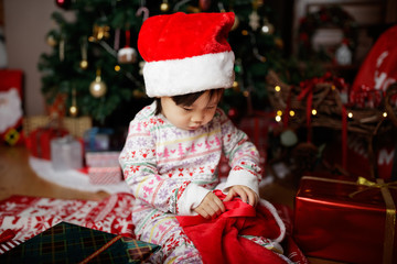 toddler baby girl wearing santa claus costume looking for gift  in front of christmas tree