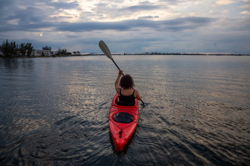 Adventurous girl kayaking in the Atlantic Ocean during a vibrant cloudy sunset. Taken in Key West,...