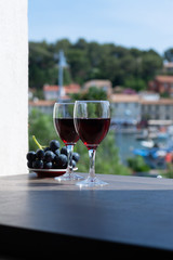 Two wine glasses with red wine served with red grape on outdoor terrace