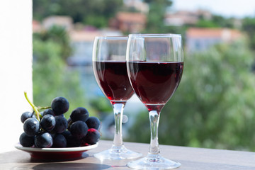 Two wine glasses with red wine served with red grape on outdoor terrace