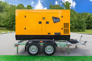 Mobile diesel charge generator for emergency electric power standing outside against green trees and blue sky - obrazy, fototapety, plakaty