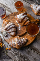 Fresh baked traditional croissant on wooden slate serving board with berries on white cloth napkin over dark brown texture background.