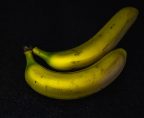 Two ripe yellow bananas on a dark background