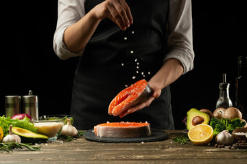The chef prepares fresh salmon fish, smorgu trout, sprinkling salt with the ingredients. Frost freezing in the air. Preparing to cook fish food. Salmon steak. Woman cook