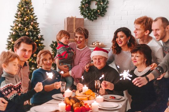 Happy Big Family At Christmas Dinner. Children Are Happy New Year Holding Sparklers In Their Hands