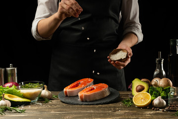 The chef prepares fresh fish salmon, trout, sprinkles with sea salt and vegetables. Horizontal photo. Concept cooking healthy and vegan cuisine, clean food, restaurants, hotel business