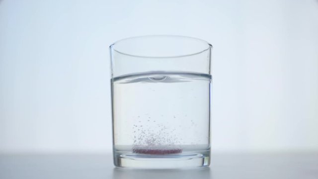 Glass of Water with Soluble Effervescent Pink Aspirin Pill with Sparklig Bubbles in Slow Motion. Healthcare and Medicine