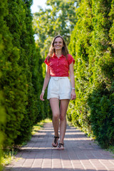 Portrait of young smiling woman in white short and red blouse walking in summer park, outdoors/Beautiful happy woman walking on the road