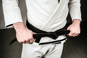 Midsection of Man in A Gi holding Black Belt tied Around His Waist.