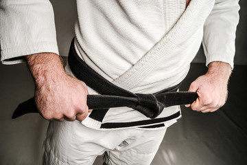 Midsection of Man in A Gi holding Black Belt tied Around His Waist.