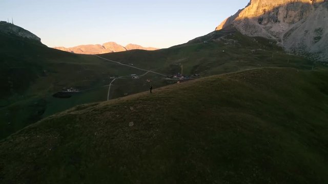 Woman hiking at the Dolomites, C4k aerial, drone shot, around a girl walking on a hill, in front of Sassolungo mountain, on a sunny, summer morning, in Tyrol, Italy