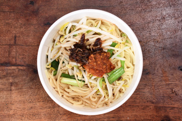 Noodles with vegetables and chili sauce in take-out  food container on wooden table  
