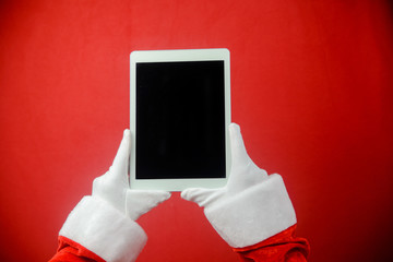 Santa showing tablet PC during holiday time, mockup electronic communications technology equipment background. Closeup image of hands working with video or photography on smart pad.