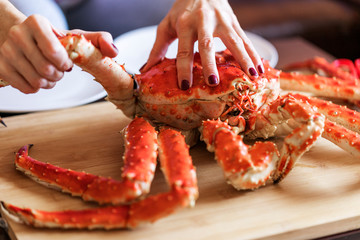 women's hands is taking leg from big red cooked crab for food © Aidman