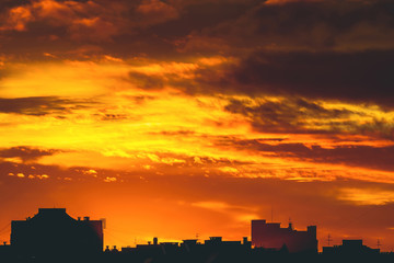 Cityscape with vivid fiery dawn. Amazing warm dramatic cloudy sky above dark silhouettes of city...
