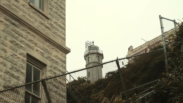 Concrete guard tower on Alcatraz island with fence foreground on cloudy day - slow moving, San Francisco, USA