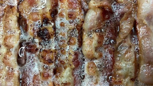 Pile of crispy bacon being fried in grease with sizzling and popping sounds