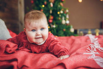 Smiling cute baby child in red dress lying on bed near new year tree