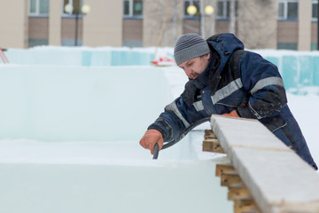 A worker-installer with a hose pours water on the ice