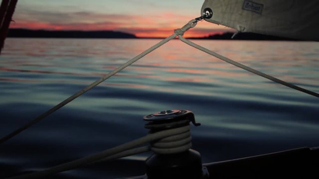 Shot during a nice boat trip with a sailing boat. Visible a blowing halyard and a winch. The red sun from the sunset reflects to the water.