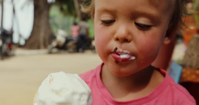 Crop closeup shot of infant boy holding waffle cone enjoying vanilla ice-cream outdoors