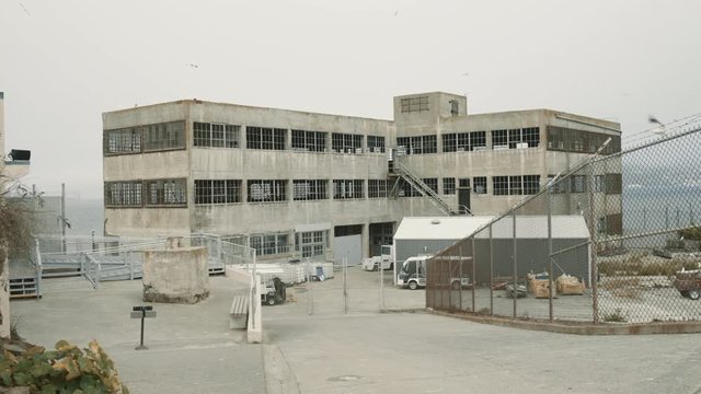 Wide Moving shot of Old abandoned concrete building with fence on Alcatraz Island at cloudy day, San Francisco, USA