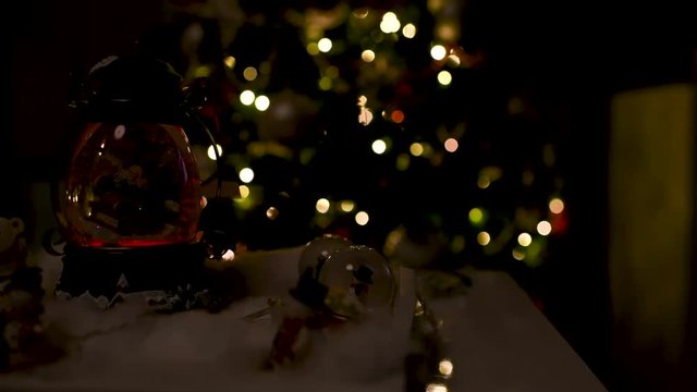 Cute Christmas decoration with snow globes on the table and lights on and off with a blurred Christmas tree in the background. Panoramic plane
