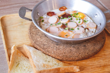 Breakfast fried eggs with sausage and toast in a small pan.