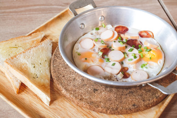 Breakfast fried eggs with sausage and toast in a small pan.