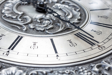 Old vintage clock with metal dial and floral embossed pattern close-up. Black clock hands...