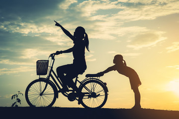 Obraz premium Silhouette of mother with her daughter and bicycle