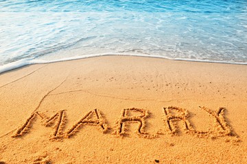 The word marry handwriting on sand beach with blue waves background.