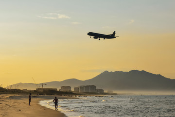 Airplane silhouette on bright sunny cloudy sky background. landing at the airport by the sea