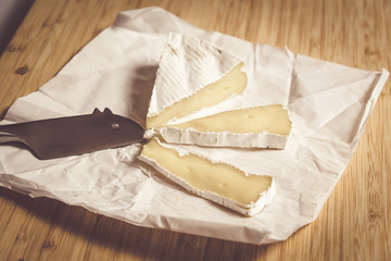 Ripe brie cheese cut into slices on paper with mouse shaped knife.