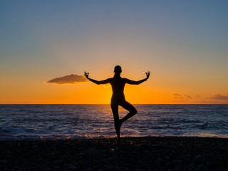 Plakat Silhouette of young woman doing exercises on the sea beach during sunset. Yoga, fitness and a healthy lifestyle