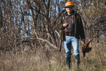 Elderly hunter with wild bird in orange hat