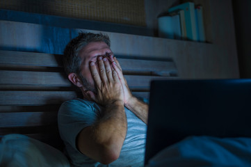attractive tired and stressed workaholic man working late night exhausted on bed busy with laptop...