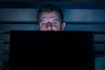 attractive and relaxed internet addict man networking concentrated late at night on bed with laptop computer in social media addiction or workaholic businessman concept