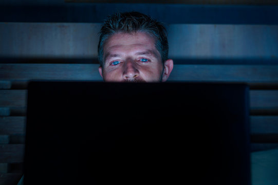attractive and relaxed internet addict man networking concentrated late at night on bed with laptop computer in social media addiction or workaholic businessman concept